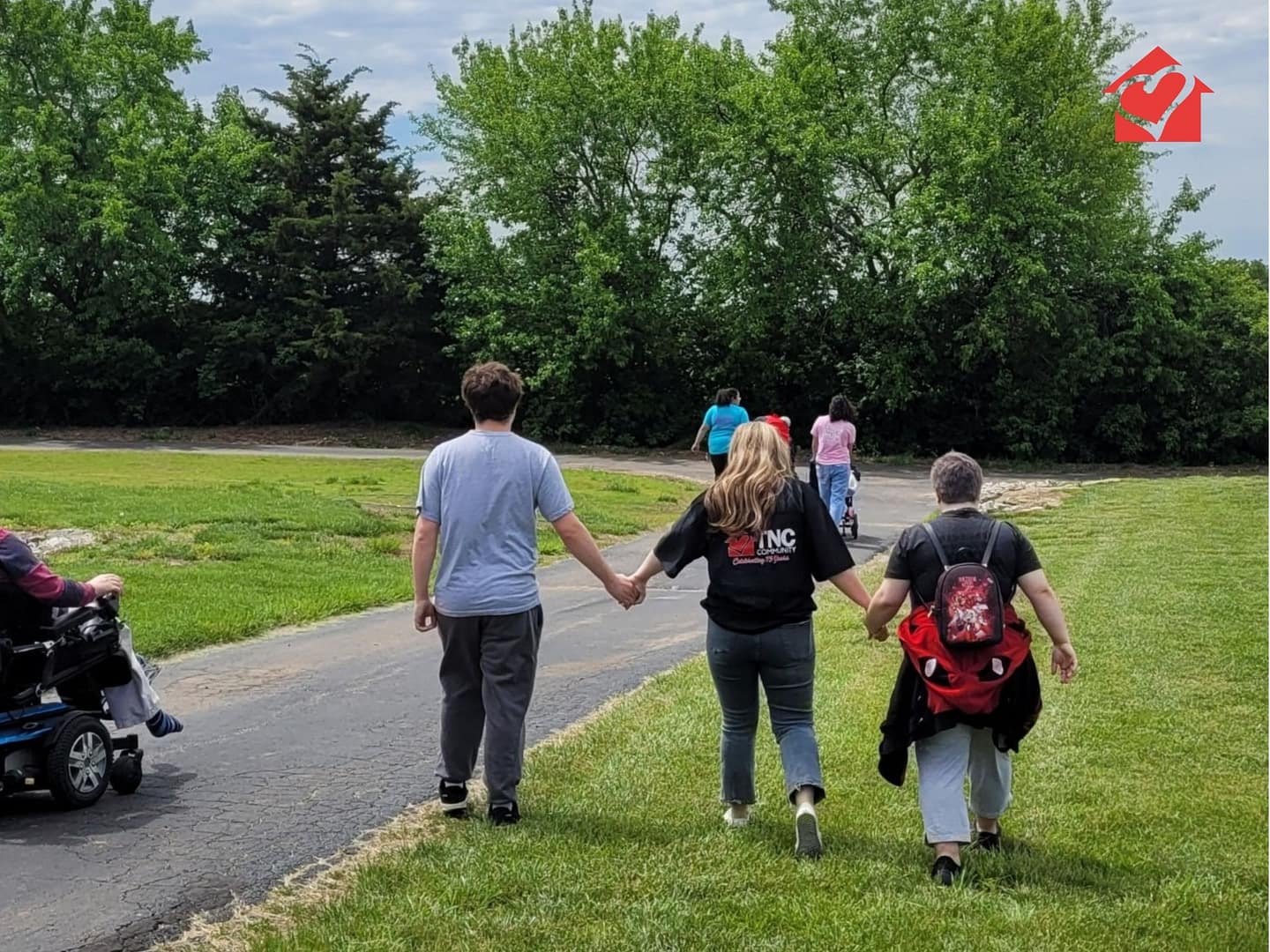 TNC Community individuals and staff holding hands on the walking path outside at Spring Fun Day